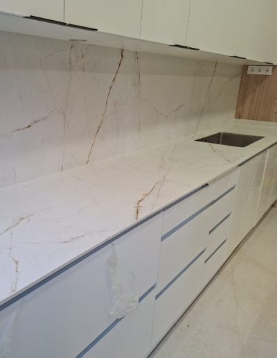 Encimera y panel de pared de porcelánico blanco con veta dorada — instalación de Mármoles y Granitos de la Vega